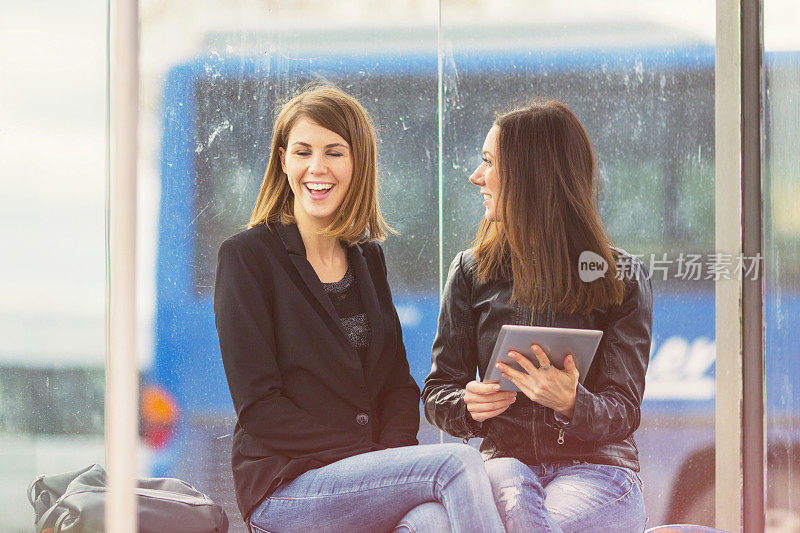 Two friends using digital tablet on bus station